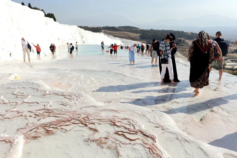 Tourist walking barefoot on the white travertine terraces of Pamukkale, Turkey with mineral-rich thermal waters